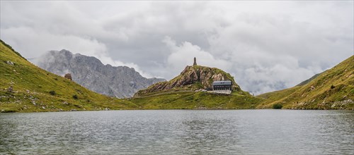 View over the Wolayersee lake to Alpenvereinshütte Wolayerseehütte, cloudy mountain landscape,