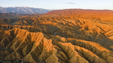 River bed runs through a landscape of eroded hills, badlands at sunset, mountain peaks of the Tian