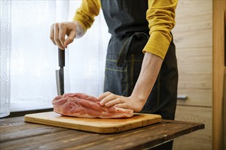 Unrecognizable man in the kitchen leans with one hand on a pork shoulder and with the other hand on