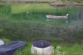 A small boat floats on a calm green lake, surrounded by grass and nature, Mindresundet, Stryn,