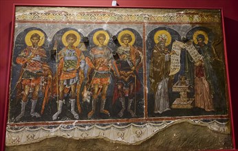 Medieval fresco depicting saints and apostles, all with glowing halos and textual writings on