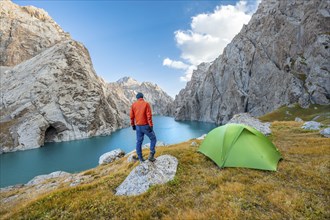 Young man with green tent at the turquoise mountain lake Kol Suu with rocky steep mountains, Kol