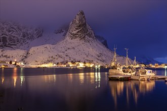 Fishing boats in fjord in front of snowy mountains, illuminated, twilight, winter, Reine,