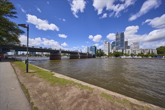 Untermainbrücke with riverside promenade, Main and skyscrapers under a blue sky with cumulus clouds