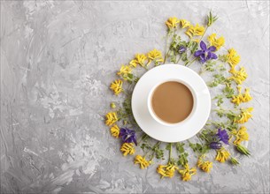 Yellow and blue flowers in a spiral and a cup of coffee on a gray concrete background. Morninig,