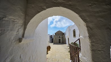 Passage through a stone arch with a view of white buildings and blue sky in the Greek monastery,