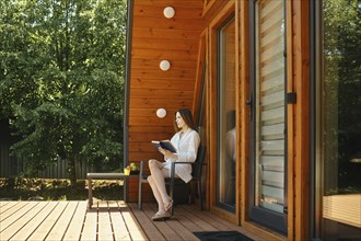 Woman relaxing outside the city reading a book on the terrace of tiny house