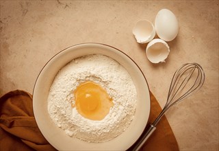 Food background, concept, plate with wheat flour, broken egg, whisk, kitchen towel, on a beige