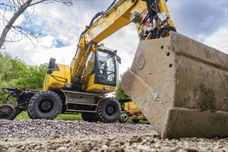 Yellow excavator on a construction site, the shovel in the foreground, cloudy sky in the