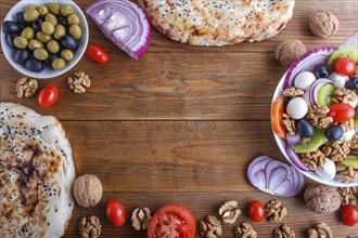 Frame made from cherry tomatoes, mozzarella cheese, olives, kiwi, onion and walnuts on brown wooden