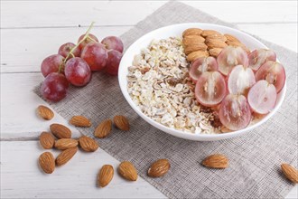 A plate with muesli, almonds, pink grapes on a white wooden background. close up