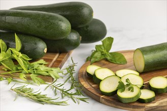 Sliced courgettes on a wooden board, with stacked courgettes and various fresh herbs next to them