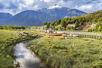 View over swampy meadows, houses and wooden boardwalk of Caleta Tortel, mountains in the back,