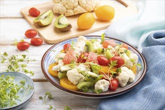 Vegetarian salad of cauliflower cabbage, kiwi, tomatoes, microgreen sprouts on white wooden