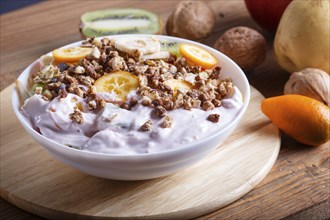 Vegetarian salad of bananas, apples, pears, kumquats, kiwi with granola and yogurt on brown woodem