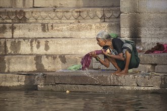 Old washerwoman washing linen in polluted water of the Ganges river at Varanasi, Uttar Pradesh,