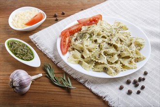 Farfalle pasta with pesto sauce, tomatoes and cheese on a linen tablecloth on brown wooden