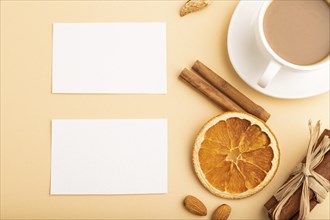 Composition of white paper business cards, almonds, cinnamon and cup of coffee. mockup on orange