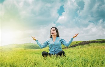 Beautiful girl meditating on the grass in a beautiful field. Portrait of relaxed young woman doing