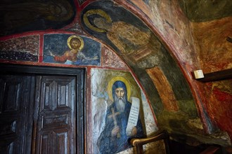 Scene of an orthodox church with religious wall paintings and a wooden door in the background,