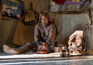 Traditional Himba woman making ochre body paint from fat and ochre, interior of the first woman's