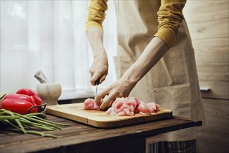 Unrecognizable man in apron slicing raw chicken fillet with kitchen knife in the kitchen