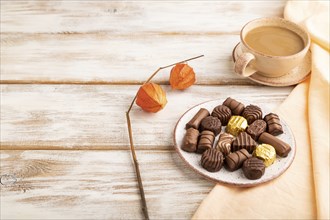 Chocolate candies with cup of coffee and physalis flowers on a white wooden background and orange