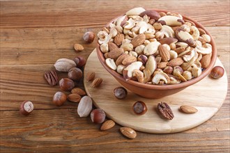 Mixed different kinds of nuts in ceramic bowl on brown wooden background with copy space. hazelnut,