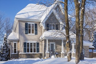 Country tan brick and vinyl cladded cottage style house facade with blue trim in winter, Quebec,