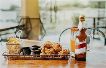 Traditional spicy chicken wings with fries and michelada accompanied with beer served on wooden