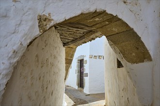 Narrow arched passageway with white walls and wooden beams in a quiet alley, Chora, Old Town,