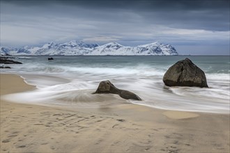 Rocks on the beach in front of snowy mountains, dark clouds, sea, spray, winter, Vikten,