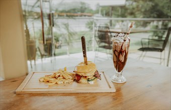 Classic burger with fries and milkshake on wooden board with copy space. Big hamburger with fries