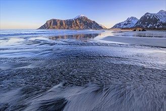 River course on the beach in front of snowy mountains, morning light, winter, Flakstadoya, Lofoten,