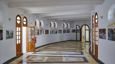 Light-flooded hallway with marble floor and wooden doors, decorated with square windows and