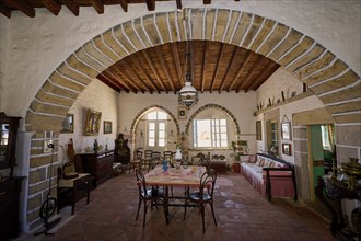 Dining room with round arch, rustic wooden floors and antique furniture. Bright windows let in