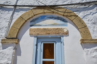 A building with a stone arch above a shutter and a painting on the façade, Chora, Old Town, Patmos,