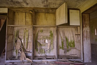 Dilapidated room with damaged wooden furniture and shelves, showing clear signs of decay and dirt