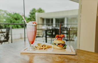 Traditional chicken burger with french fries and strawberry milkshake on restaurant table.