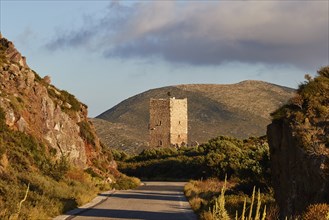 The view of a historic tower on a street, surrounded by mountains in the evening light, residential