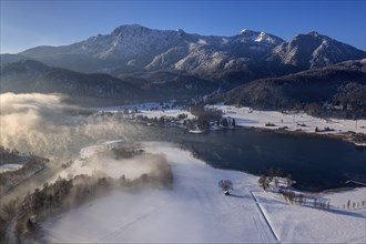 Aerial view of a lake in front of mountains in winter, snow, fog, morning light, view of