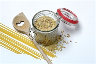 Fregola in wooden spoon and glass container with spaghetti, pasta variety from Sardinia, Italy,