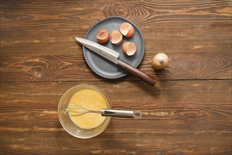 Top view of rustic wooden table with a bowl with beaten eggs and a plate with broken eggshells and