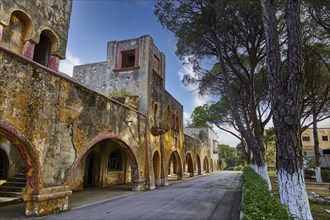 A long corridor of a historic, dilapidated building with arches and trees along the street, Italian