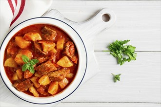 Potatoes stewed with meat, in tomato sauce, with spices and herbs, no people, on a white table