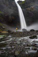 Young man with yellow jacket standing in front of waterfall, Haifoss and Granni waterfall at a