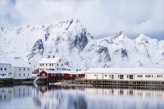 Rorbuer huts of Hamnoy at the fjord, snowy mountains in the background, Hamnoy, Reine, Moskenesoya,