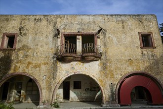 The dilapidated façade of a historic building with a yellow wall, several windows and decorative