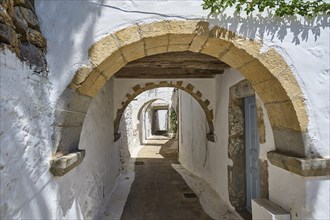 A long, narrow corridor with stone arches and white walls, typical Greek historical style, Chora,