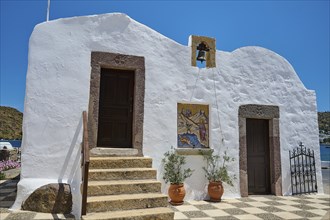 White building in traditional Greek style with staircase, two doors and bell, under blue sky and in